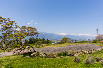 小さな橋と北アルプスを望むあづみ野池田クラフトパークの春風景