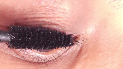 Young Indian girl with brown eyes applies black mascara on long eyelashes. Female paints artificial lashes with brush on blurred background macro, 4K resolution footage - Powered by Adobe