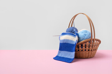 Blue and white knitting balls in basket with knitting needles and knitted scarf on pink background....