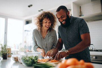 Young Couple Laughing While Preparing Meal Prep Bowls in Bright Modern White Kitchen with Natural Light