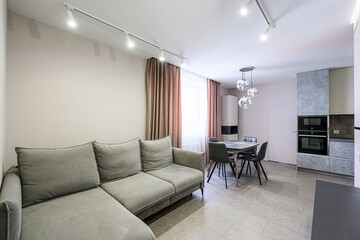 cozy living space with a gray sofa, dining table set, and kitchen area. Soft lighting and neutral tones create a welcoming atmosphere