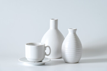 White coffee cup and saucer, white vases on a white background.