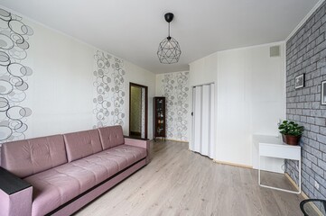 cozy living room with a mauve sofa, patterned wallpaper, geometric pendant light, and a brick...