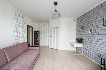 Cozy living room with a mauve couch, geometric light fixture, faux brick wall, and light wood floors