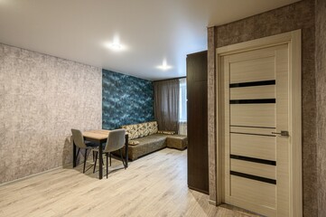 cozy living room features a dining area, sofa, and decorative wallpaper, illuminated by ceiling lights and natural light