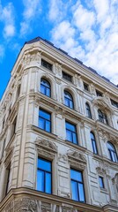 Obraz premium Ornate, light beige building facade with arched windows against a partly cloudy sky