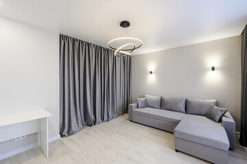 Modern living room with a grey sofa, curtains, and a unique ring chandelier. Minimalist design with...