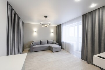 Modern living room with a grey sofa, curtains, and a unique ring chandelier. Minimalist design with light wood floors and neutral walls
