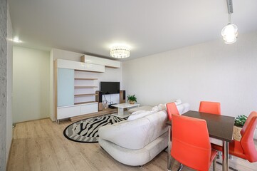 bright living room features a white couch, orange chairs, a dark table, and a modern entertainment center with a TV. A zebra-patterned rug adds a stylish touch