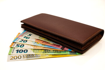 Multiple Euro Banknotes Spread Out. Closed Brown Leather Wallet with Fanned Euro Banknotes on White...