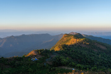 A beautiful sunset appears behind the mountains of Mae Hong Son, Thailand, casting a warm glow that...