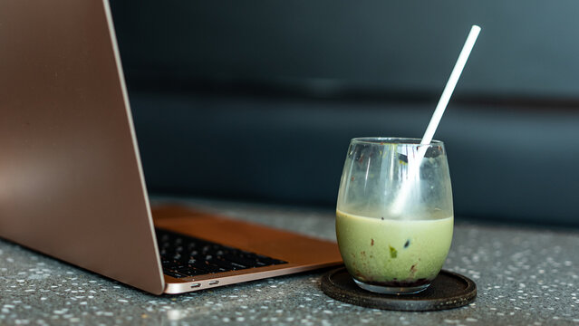 A modern workspace with a sleek laptop beside a glass of iced matcha latte on a table, blending productivity and relaxation in a cozy atmosphere.