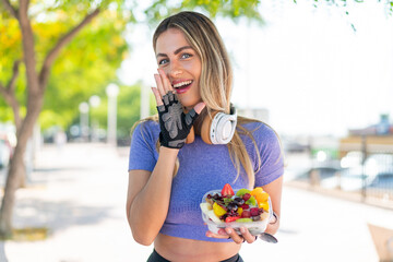 Young pretty sport woman holding a bowl of fruit at outdoors whispering something
