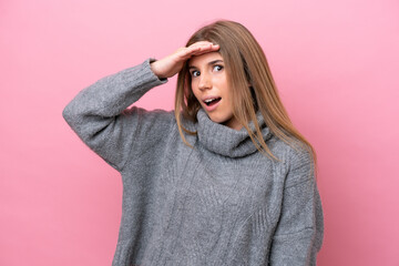 Young caucasian woman isolated on pink bakcground doing surprise gesture while looking to the side