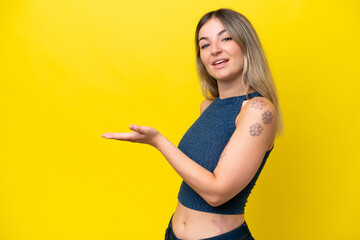 Young Rumanian woman isolated on yellow background presenting an idea while looking smiling towards