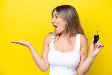 Young woman holding car keys isolated on yellow background with surprise facial expression