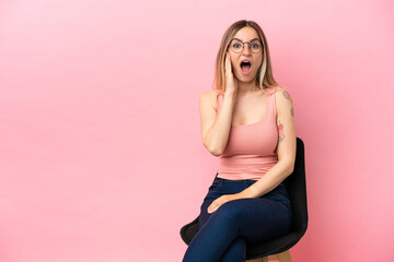 Young woman sitting on a chair over isolated pink background with surprise and shocked facial...