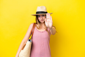 Fototapeta premium Young caucasian woman holding a beach bag isolated on yellow background making stop gesture