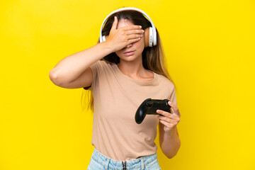 Young caucasian woman playing with a video game controller isolated on yellow background covering...