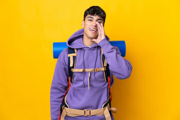 Young mountaineer man with a big backpack over isolated yellow background shouting with mouth wide...
