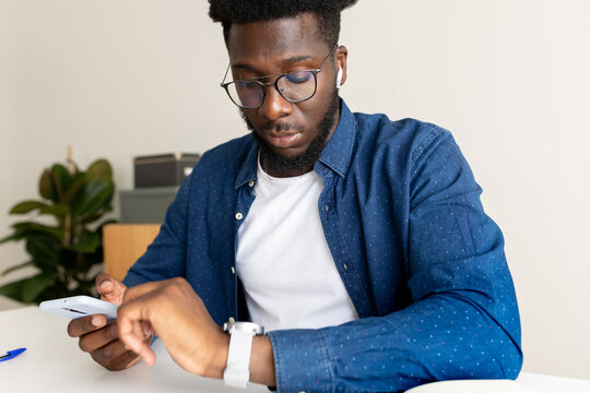 Happy African American man looking at smart watch at home office.