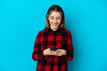 Young caucasian woman isolated on blue background sending a message with the mobile