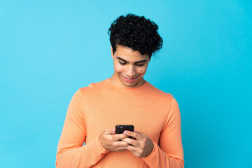Venezuelan man isolated on blue background sending a message or email with the mobile