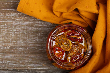 Flat lay photo of a glass jar with sun dried red and yellow cherry tomatoes in olive oil and with...