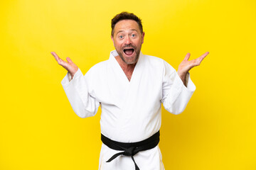 Middle age caucasian man doing karate isolated on yellow background with shocked facial expression