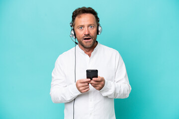 Telemarketer caucasian man working with a headset isolated on blue background surprised and sending...