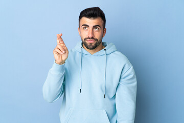 Fototapeta premium Caucasian man over isolated blue background with fingers crossing and wishing the best
