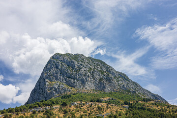 Picturesque view of rocky mountain with green forest slopes under blue sky with clouds. Nature landscape on sunny summer day. Viter mountain near Zaostrog village, Makarska Riviera, Dalmatia, Croatia.