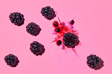 Smashed blackberry with juice and whole blackberries next to it on pink background