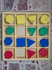 Colorful geometric shapes arranged in a wooden grid against a textured wall background.