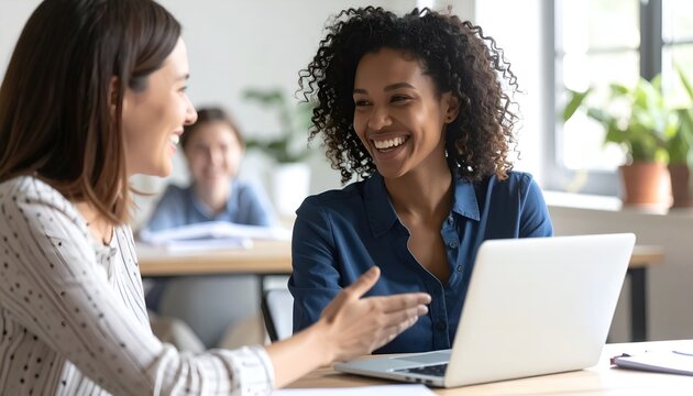 Close up happy young african american businesswoman using laptop with laughing female mentor in coworking boardroom at meeting. Smiling diverse woman managers. Detailed high quality image.