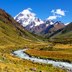 Fototapeta premium Serene mountain valley with a meandering river flowing towards a snow-capped peak under a clear blue sky