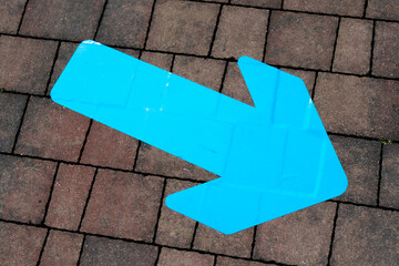 Bright blue directional arrow painted on outdoor pavement bricks, pointing forward and guiding path...