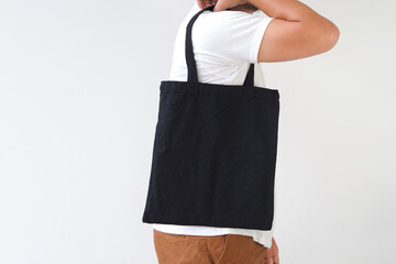 Young man hand holding black canvas tote bag on white background. Reusable eco bag for shopping. Eco friendly concept. Mockup for you designs.