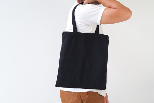 Young man hand holding black canvas tote bag on white background. Reusable eco bag for shopping. Eco friendly concept. Mockup for you designs.