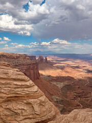 Mesa Arch in Canyonlands National Park, Utah, with rugged desert cliffs and red rock formations beneath a partly cloudy sky.
