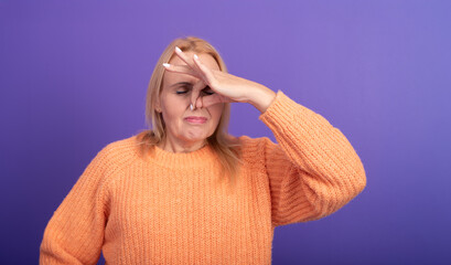Mature woman showing expression of disgust by pinching her nose, reacting to foul odor. Orange...