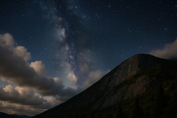 Fototapeta premium A tranquil night sky blanketed with stars above a majestic mountain, where clouds drift lazily across the horizon
