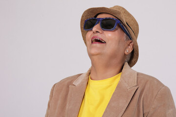 Indian stylish senior woman wearing sunglasses and hat posing confidently against grey background