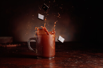 Pieces of dark chocolate fall into a glass of cocoa drink.