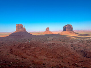 Monument Valley desert panorama with towering sandstone buttes under a bright blue sky.