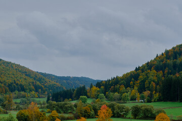 A picturesque autumn landscape. Green and yellow-orange trees cover the hills, with fields and...