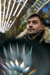 Close-up of a man in a black winter jacket with a fur hood against a background of geometric light patterns. Urban night, creative atmosphere, modern street style, autumn mood