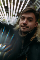 Close-up of a man in a black winter jacket with a fur hood against a background of geometric light patterns. Urban night, creative atmosphere, modern street style, autumn mood