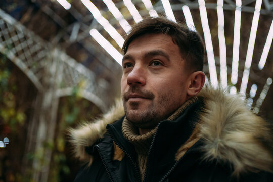 Fototapeta Close-up of a man in a black winter jacket with a fur hood against a background of geometric light patterns. Urban night, creative atmosphere, modern street style, autumn mood