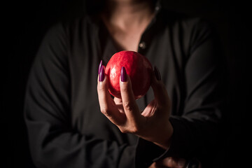 Image of a witch holding an apple in her hand, black background.